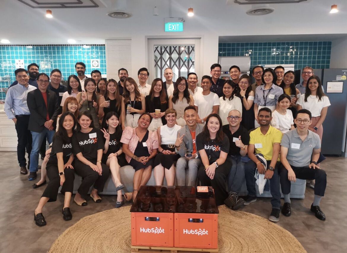 A large group of HubSpot community members and the Azend team at a HubSpot community event, seated around HubSpot-branded crates